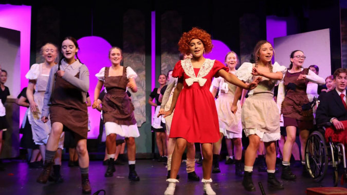 Eine Frau in rotem Kleid steht mit weiteren Darstellern auf der Bühne während einer Aufführung am Clonfert College.