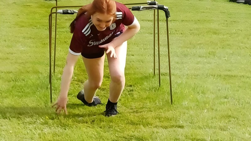 Eine Person in Sportkleidung biegt sich auf dem Sportfeld des Clonfert College vor einer grasbewachsenen Landschaft.