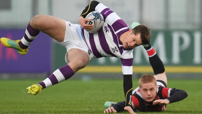 Ein Rugbyspieler in lila-weiß gestreiftem Trikot wird auf dem Spielfeld am Clongowes Wood College getackelt.