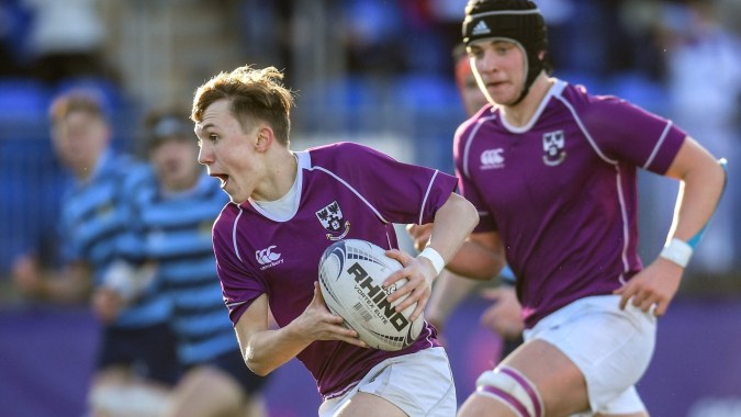 Zwei Rugbyspieler in lila Trikots spielen ein intensives Spiel auf dem Feld des Clongowes Wood College.