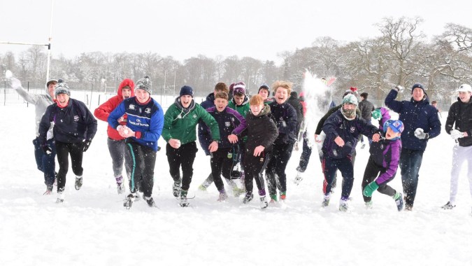 Schüler des Clongowes Wood College gehen gemeinsam auf einem verschneiten Weg zwischen kahlen Bäumen.