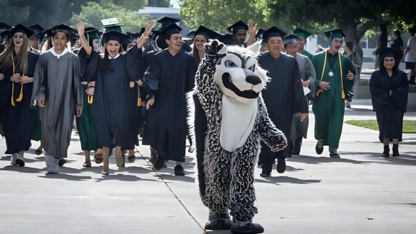 Eine Gruppe von Absolventen des Clovis Unified School District trägt akademische Kleidung und geht auf einem Campusweg mit Bäumen.
