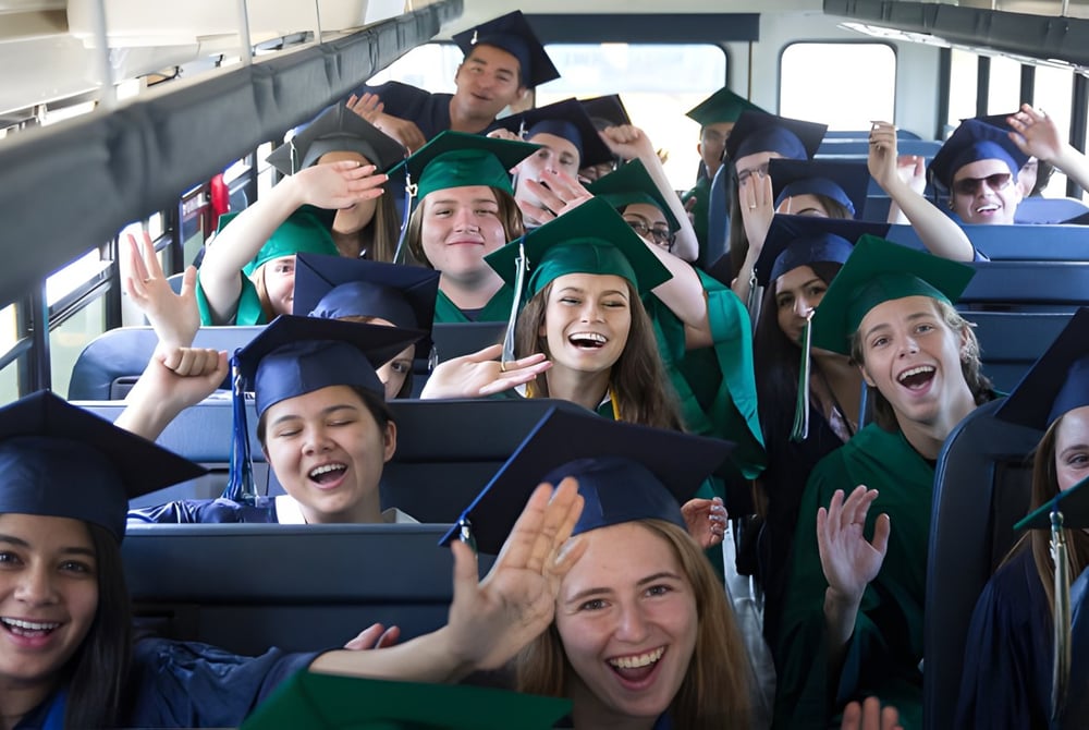 Absolventinnen und Absolventen des Clovis Unified School District feiern im Bus ihre Graduierung in akademischer Kleidung.