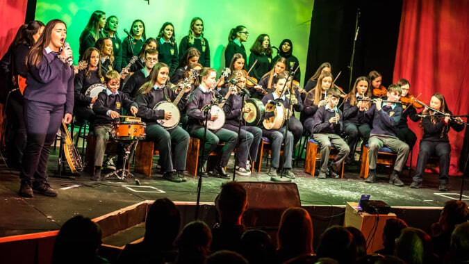 Schüler der Cnoc Mhuire Secondary School spielen gemeinsam verschiedene Musikinstrumente auf der Bühne.