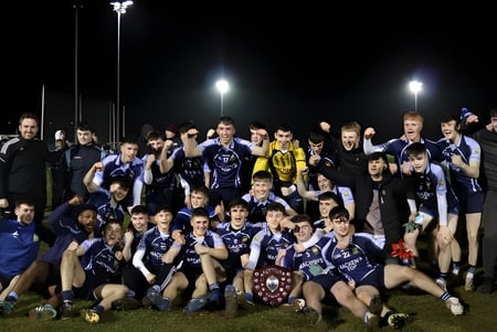 Die Sportmannschaft der Cnoc Mhuire Secondary School posiert gemeinsam auf dem Sportplatz bei Nacht.