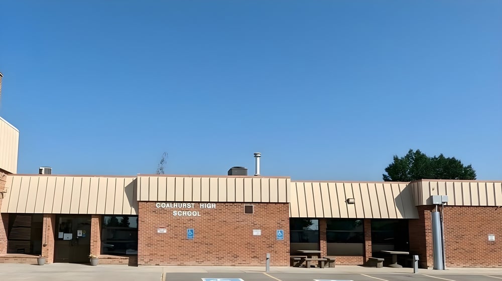 Das Backsteingebäude der Coalhurst High School steht umgeben von Bäumen unter klarem blauem Himmel.