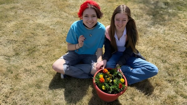 Zwei Schülerinnen der Coalhurst High School sitzen auf dem Gras und halten einen bunten Korb mit Pflanzen.