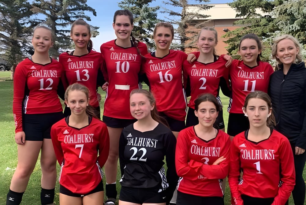 Eine Gruppe junger Schülerinnen der Coalhurst High School posiert gemeinsam im Freien auf einer Wiese mit Bäumen im Hintergrund.