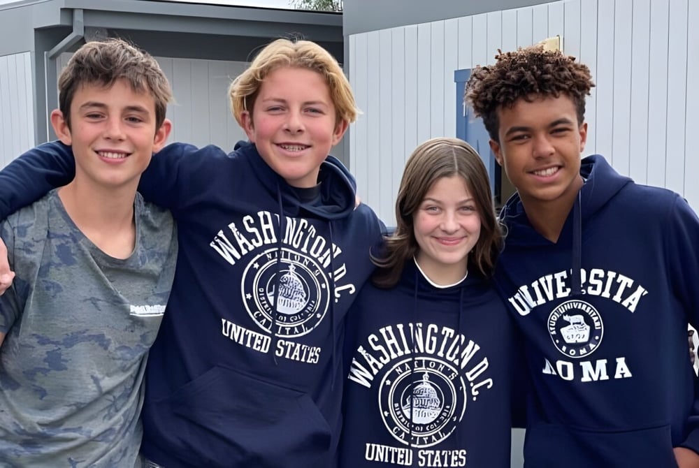 Vier Schülerinnen und Schüler stehen vor dem Gebäude der Coastal Christian School und lächeln in die Kamera.