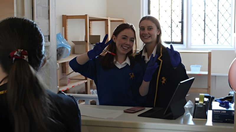 Zwei Schülerinnen der Cobham Hall School stehen hinter einer Theke und unterhalten sich mit einer Person außerhalb des Bildes.