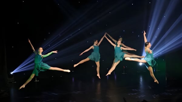 Eine Gruppe von Tänzerinnen und Tänzern der Cobham Hall School führt auf einer dunklen Bühne eine synchronisierte Luftakrobatik auf.