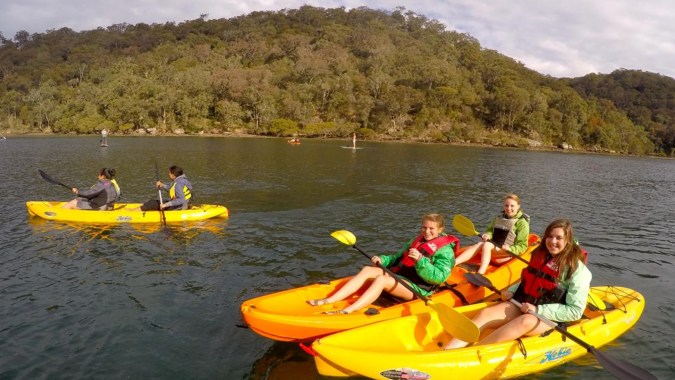Schüler des Coláiste an Chreagáin paddeln mit bunten Schlauchbooten auf einem See vor bewaldeten Hügeln.