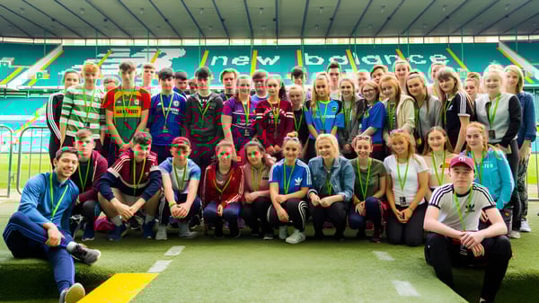 Eine Gruppe Schülerinnen und Schüler steht auf dem Sportfeld von Coláiste an Chreagáin mit Sporttrikots und Freizeitkleidung.