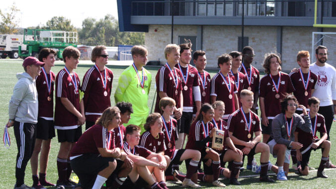 Schülerinnen und Schüler des Coláiste Bhaile Chláir stehen mit Trophäen auf dem Fußballfeld.