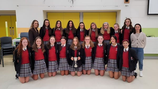 Eine Gruppe Schülerinnen in roten und schwarzen Uniformen steht gemeinsam auf dem Campus der Coláiste Bhaile Chláir.