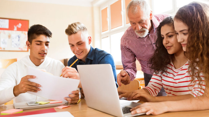 Schüler und eine Lehrerin arbeiten gemeinsam an einem Laptop im Klassenraum des Coláiste Bhaile Chláir.