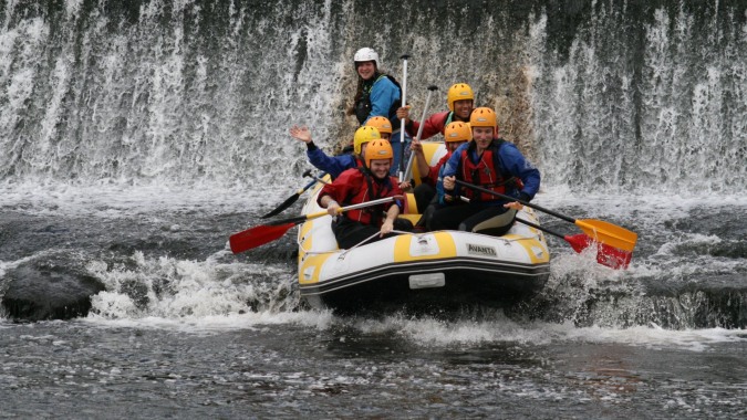 Schüler der Colaiste Chiarain Athlone beim Wildwasser-Rafting vor einem großen Wasserfall.