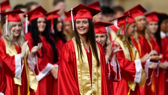 Eine Gruppe Absolventen in roten und goldenen Talaren steht gemeinsam und lächelt auf dem Campus von Coláiste Chill Mhantáin.