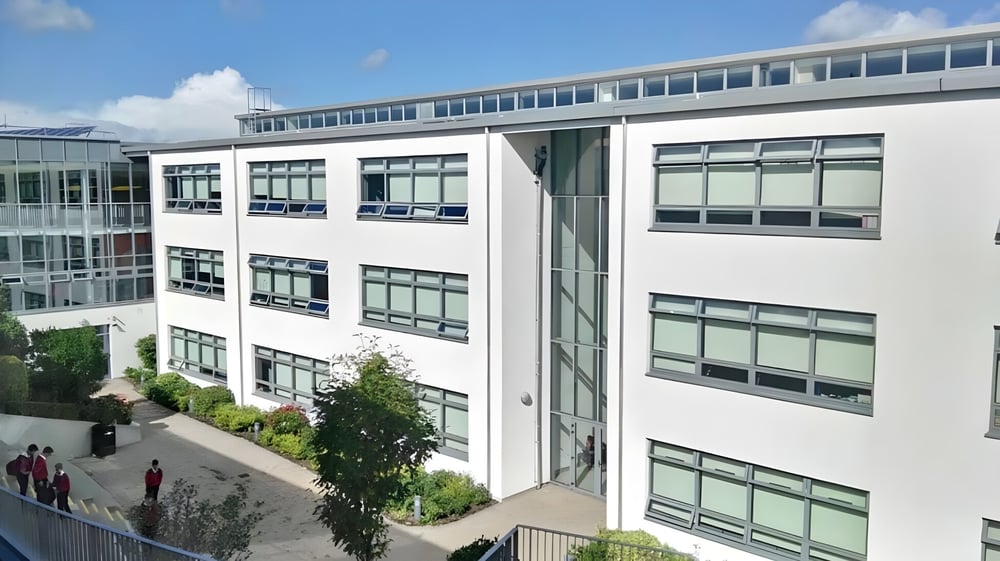 Das mehrstöckige Gebäude von Coláiste Chill Mhantáin mit Glasfassade und umgebendem Grün ist zu sehen.