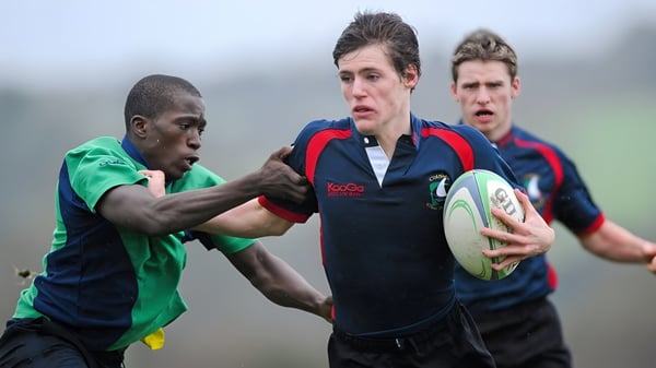 Zwei Rugbyspieler der Coláiste Chill Mhantáin führen einen Tackle auf dem Rasenfeld aus.
