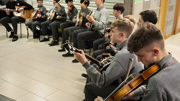 Schülerinnen und Schüler spielen verschiedene Musikinstrumente wie Gitarren und Geigen im Musikunterricht an der Coláiste Choilm.