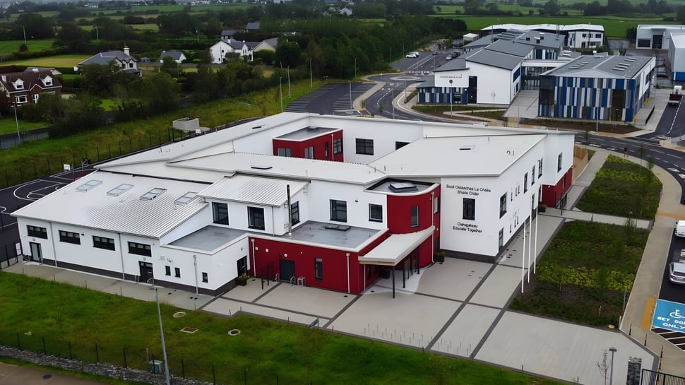 Das moderne mehrstöckige Gebäude von Coláiste Chríost Rí steht umgeben von einer Grünfläche und weiteren Gebäuden im Hintergrund.