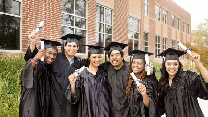 Eine Gruppe von Absolventinnen und Absolventen in Abschlusskleidung steht vor einem Backsteingebäude auf dem Campus der Coláiste Éamann Rís.