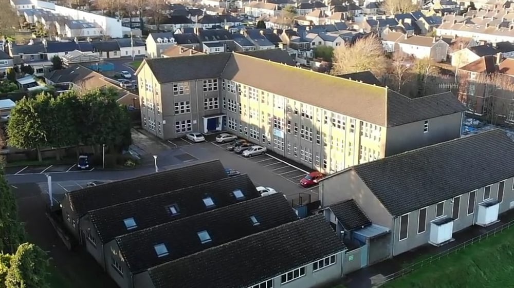 Mehrstöckiges Schulgebäude von Coláiste Éamann Rís in einer urbanen Umgebung mit umgebenden Wohn- und Geschäftsgebäuden.