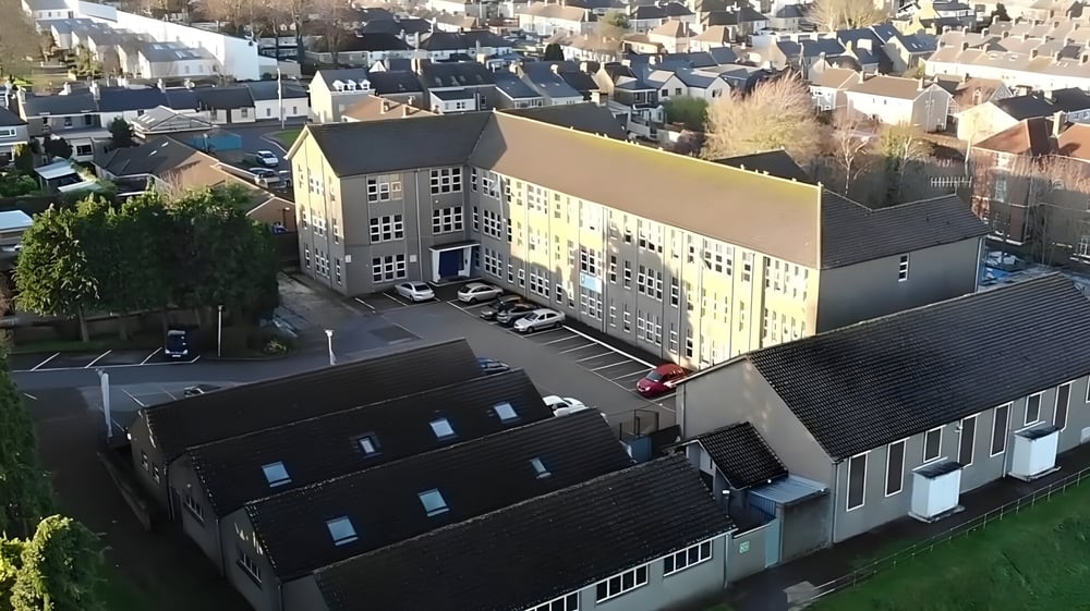 Das mehrstöckige Hauptgebäude der Coláiste Éamann Rís steht im Vordergrund vor einer Stadtkulisse.