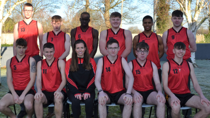 Eine Gruppe Schüler in roten Trikots posiert für ein Teamfoto im Freien auf dem Gelände der Coláiste Éamann Rís.