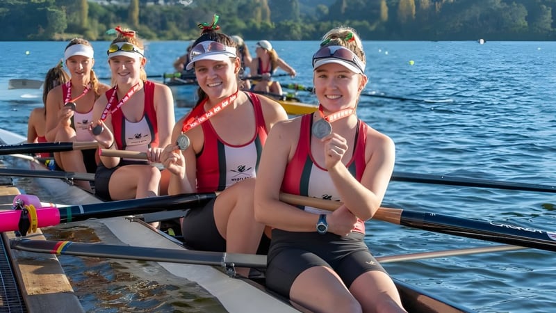 Schülerinnen der Coláiste Íosagáin sitzen in einem Ruderboot auf einem See, umgeben von Wald.