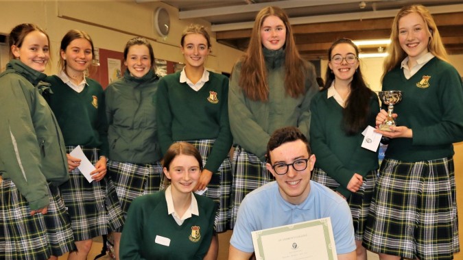 Eine Gruppe Schülerinnen in Schuluniformen posiert mit einem Pokal auf dem Campus der Coláiste Íosagáin.