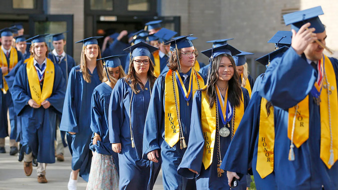 Eine Gruppe von Absolventinnen und Absolventen der Coláiste Mhuire (Ballygar) geht in blauen und gelben Talaren vor dem Universitätsgebäude.