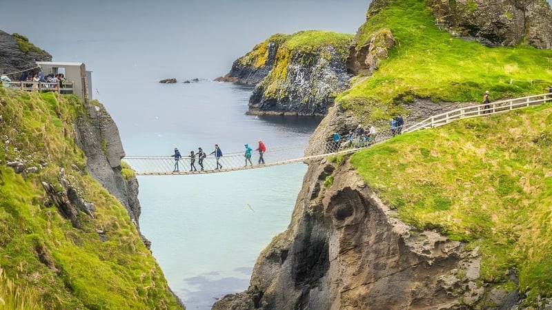Schüler der Coláiste Mhuire Ballygar überqueren eine Hängebrücke über einer Küstenlandschaft mit Klippen und Wasser.