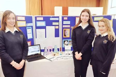 Drei Schülerinnen in Schuluniformen stehen vor einem Schaukasten im Schulgebäude der Coláiste Mhuire Ballymote.