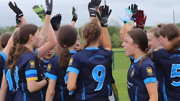 Eine Gruppe junger Fußballspielerinnen in blauen und weißen Trikots feiert gemeinsam auf dem Sportplatz der Coláiste Mhuire (Ballygar).