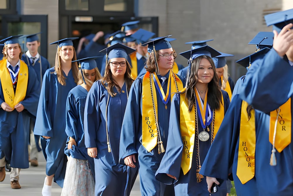 Eine Gruppe von Absolventinnen und Absolventen der Coláiste Mhuire (Ballygar) in blauen und gelben Talaren geht gemeinsam vor dem Universitätsgebäude.