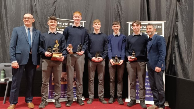 Eine Gruppe von Personen steht gemeinsam vor einem Logo auf dem Campus der Coláiste Mhuire Mullingar.