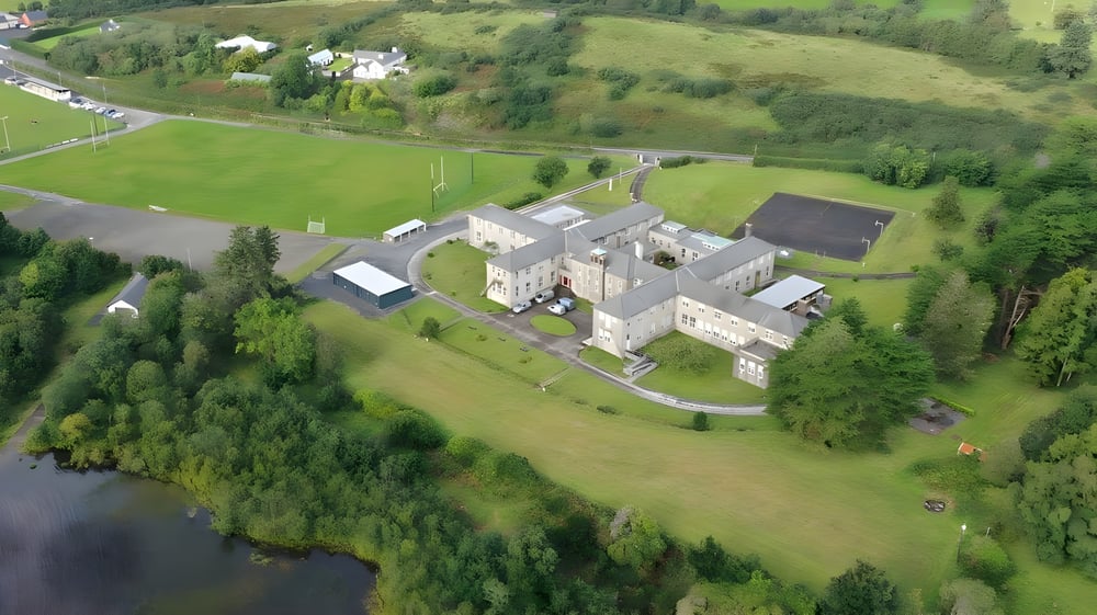 Ein ländliches Panorama mit traditionellen Steingebäuden und grünen Feldern auf dem Gelände von Colaiste Mhuire Tourmakeady.