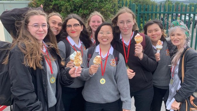 Eine Gruppe Absolventinnen der Colaiste Muire Cobh im Freien mit Abschlusskappen und -roben hält stolz ihre Diplome.