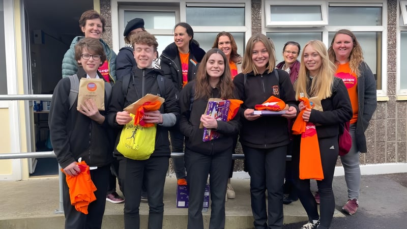 Eine Gruppe Schülerinnen und Schüler steht vor einem Gebäude auf dem Campus der Colaiste Muire (Cobh) in bunter Kleidung zusammen.