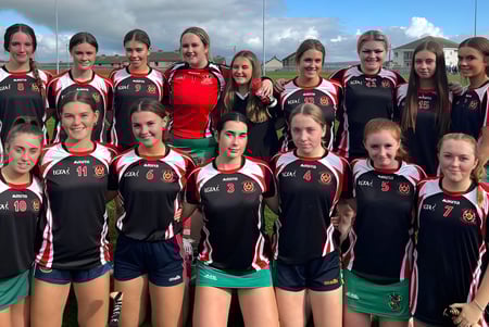 Eine Gruppe junger Sportlerinnen posiert auf dem Sportfeld von Colaiste Muire (Cobh) vor bewölktem Himmel.