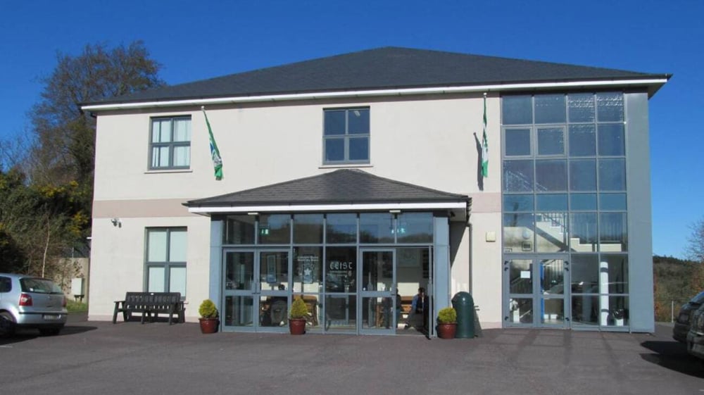 Das moderne Schulgebäude der Coláiste Muire Crosshaven mit großen Glasfenstern und Eingang unter blauem Himmel.
