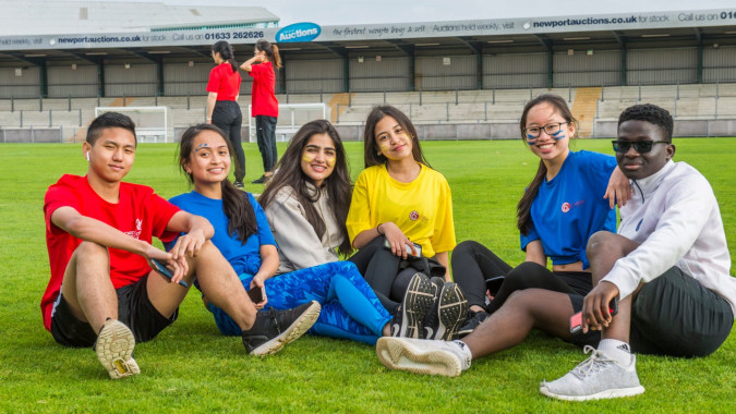 Eine Gruppe Schülerinnen und Schüler von Coláiste Muire Crosshaven sitzt auf einer Wiese vor einem Sportstadion.