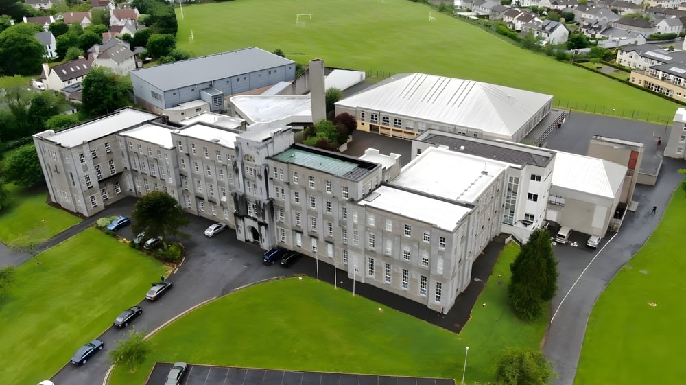 Das große mehrstöckige Gebäude der Colaiste Muire Mathair steht auf einer Wiese, umgeben von Grünflächen und kleineren Gebäuden.