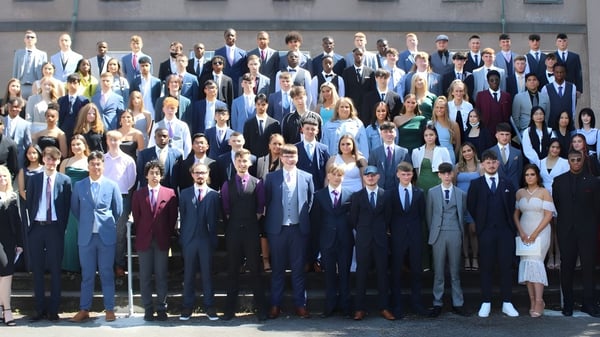 Eine Gruppe von Menschen in formeller Kleidung steht gemeinsam im Freien vor einem Gebäude auf dem Campus der Colaiste Muire Mathair.
