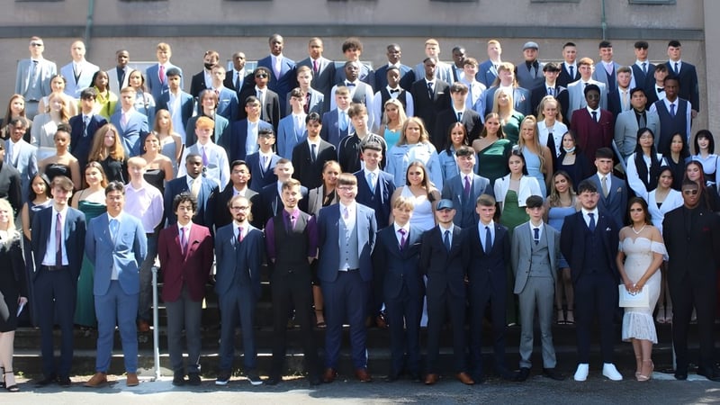 Eine Gruppe von Menschen in formeller Kleidung steht gemeinsam im Freien vor einem Gebäude auf dem Campus der Colaiste Muire Mathair.