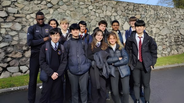 Eine Gruppe Schüler in Schuluniformen steht vor einer Steinmauer auf dem Gelände der Colaiste Muire Mathair.
