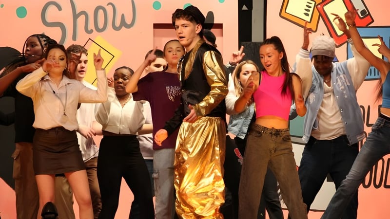 Eine Gruppe von Schülerinnen und Schülern steht vor einem Hintergrund mit dem Schriftzug Show auf dem Campus der Colaiste Muire Mathair.