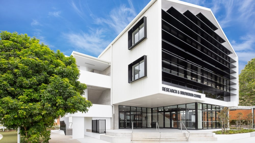 Das moderne Gebäude der Coláiste Naomh Cormac steht umgeben von grüner Vegetation unter klarem blauem Himmel.